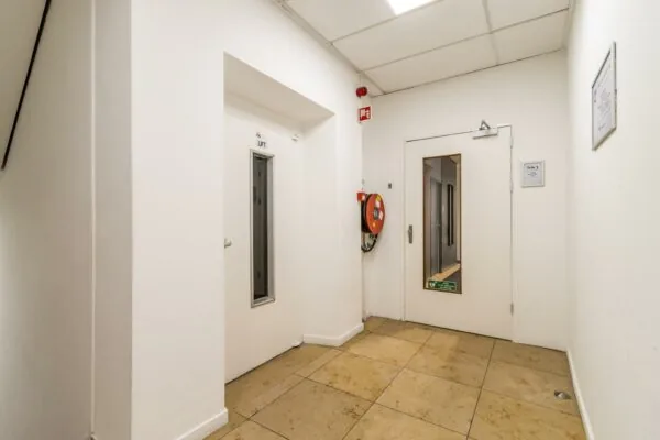 Witte gang in een kantoorpand aan de Jan van Eycklaan met een liftdeur, brandhaspel en toegangsdeur met raam.